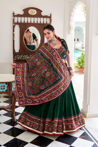 Woman in a traditional green and multicolored saree standing in a room with a checkered floor.